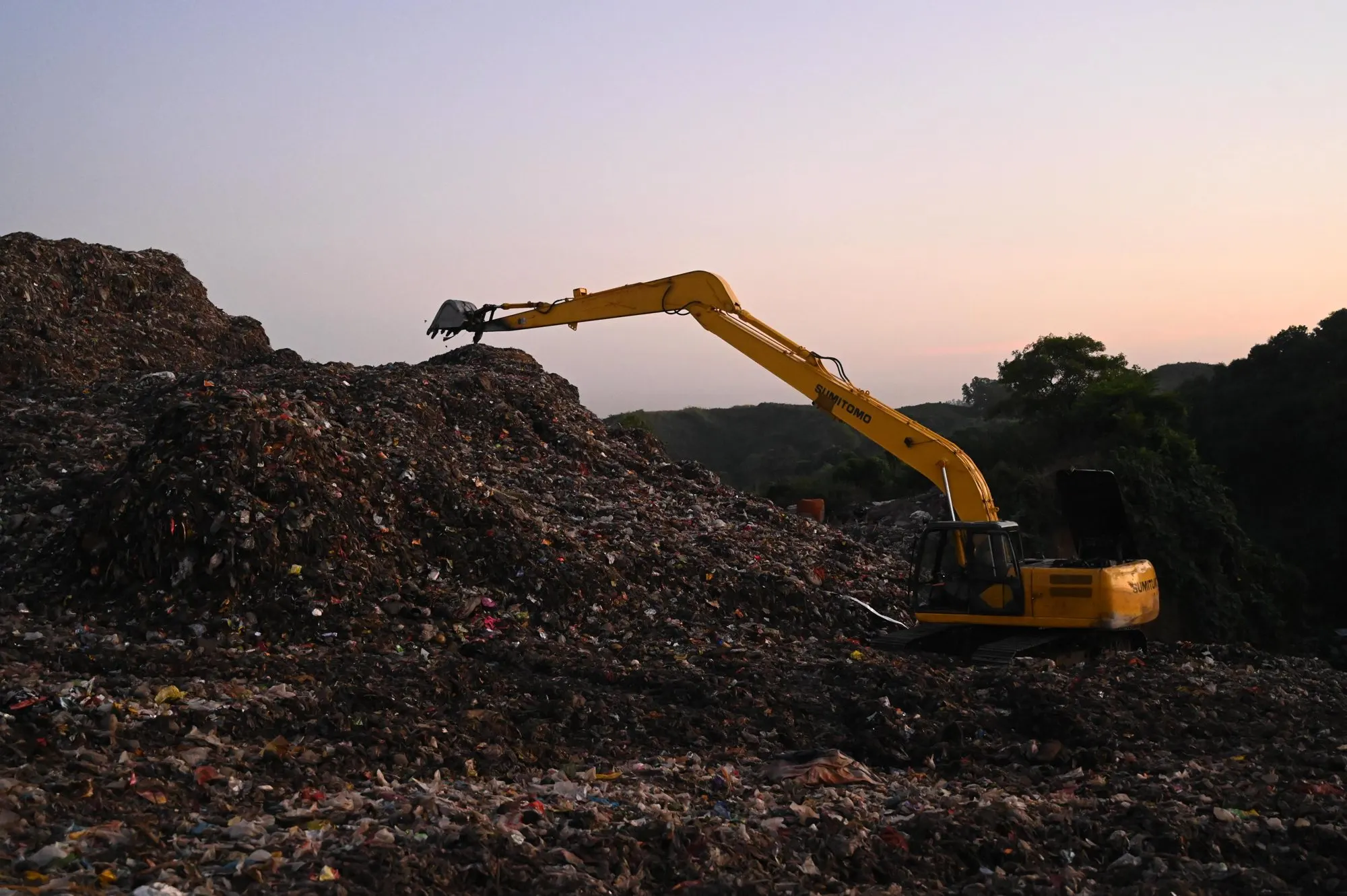 Una ruspa al lavoro su una discarica al tramonto